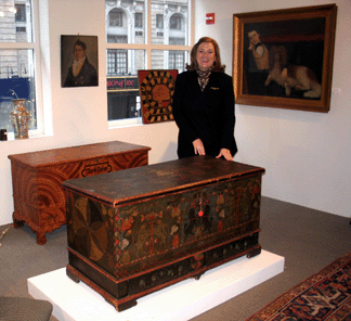 LaGina Austin of Skinner's Americana team with some of the day's top lots. The 1796 Berks County, Penn., dower chest with black unicorn decoration sold to Olde Hope Antiques on behalf of a client for $440,000 ($25/35,000). The New Hope, Penn., dealers' other purchase was the cover lot, right, an attributed Joseph Whiting Stock oil on canvas portrait of a boy and his spaniel, $31,725. Inscribed "Jacob Hubner 1815,” the Schwenkfelder dower chest from Pennsburg, Penn., went to the phone for $30,550. Above it, the portrait of Martha's Vineyard sea captain Bartlett Mayhew fetched $35,250. On the windowsill, the Nineteenth Century "Game of The Goose” brought $16,450. —Laura Beach photo
