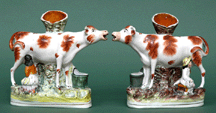 Pair of Staffordshire large cowform spill vases each base inscribed Milk Sold Here and molded against a tree trunk vase fronted by thistle branch 6325