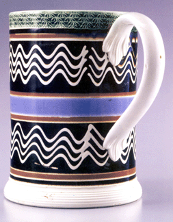 This quartcapacity pearlware mug just over 6 inches tall was probably made by the firm of Enoch Wood amp Sons Burslem Staffordshire circa 1830 The turner exercised considerable skill in trailing the slip from a singlecolor slip cup fitted with four goose quills through which the white slip was trailed onto the black slip fields as the mug revolved on the horizontal lathe The center band is bright blue and the distinctive rouletted rim is colored with copper oxide in the glaze