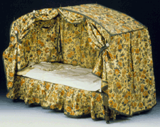 A small doll bed with its original rollerprinted cotton bed hangings