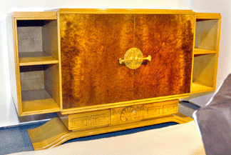 This commode decorated by T.H. Robsjohn-Gibbings seen at Antiquities, Fort Lauderdale, Fla., was made of carved harewood and amboyna and featured doors centered with elaborately designed brass hardware.