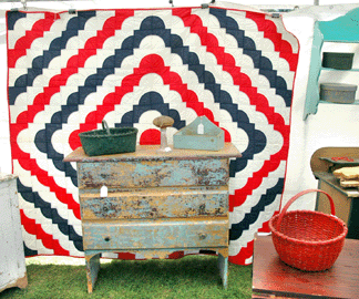 From Timber River, New Brunswick, Canada, Cathy Consentino placed a colorful around-the-world quilt that had been made for the Virginia US bicentennial behind a handsome Nineteenth Century three-drawer chest and flanked it with a green basket from Maine. ⁈ertan's Antique Shows