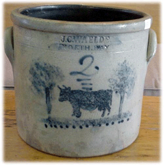 The crock decorated with a cow and trees was made by J.C. Wealde of nearby North Bay, N.Y., and sold for $3,200 in spite of condition problems.