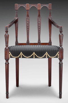The design of the 1801 Santo Domingo mahogany armchair is based on a plate from Thomas Sheraton's 1793 Cabinet-Maker and Upholsterer's Drawing Book and is one of 12 made for the parlor of the Peirce Nichols House. McIntire carved the delicate black splats with bellflowers suspended from bows and terminating in rosettes. It is upholstered with black-striped cloth woven from the tail and mane of a horse.