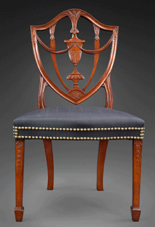 McIntire carved the shield form back of the Santo Domingan mahogany side chair with urns and swags and sheaves of wheat. He gave the square legs cascades of bellflowers. It is upholstered with black striped hair cloth, woven from the tail and mane of a horse.