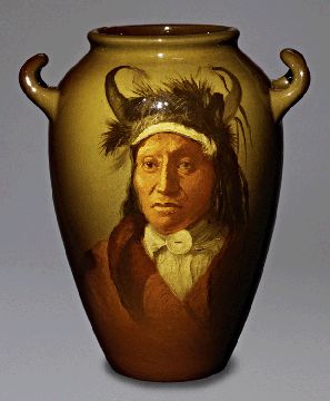 Displaying his Plains finery with an Assiniboine war bonnet with curved horns and feather fluffs and a trade blanket coat, Wets It is depicted in this portrait vase decorated by Frederick Sturgis Laurence, 1900. The Rookwood Pottery Company, collection of James J. Gardner.