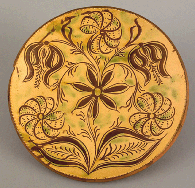 A Bucks County, Haycock Township, Penn., sgraffito decorated redware plate attributed to Conrad Mumbouer, circa 1815, was adorned with tulip vine and stylized floral pinwheel decoration and sold for $76,050.