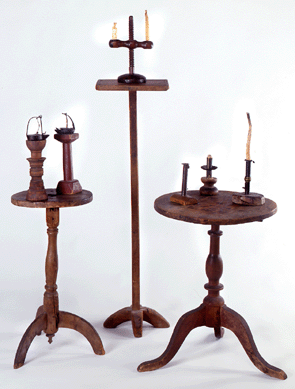 Three pine candlestands hold an array of lighting devices. The stand on the left, circa 1740, is from eastern central Massachusetts; the tall one is a coastal New Hampshire piece from about 1790‱810, and the one on the right is circa 1750‱780 from central eastern Connecticut.