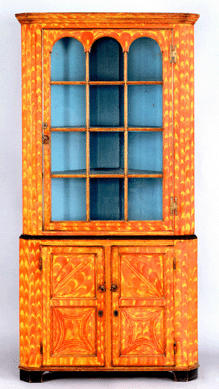 A Pennsylvania painted poplar two-part corner cupboard dating from the early Nineteenth Century, retaining the original vibrant yellow and orange decorated surface, 81 inches high, 37½ inches wide, sold for $49,140, above the high estimate of $35,000. The provenance lists Nancy and James Glazer.