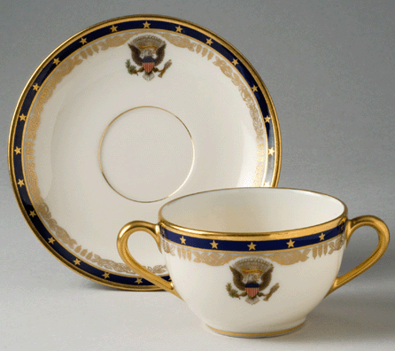 The bouillon cup and saucer were part of the 1,722-piece state service ordered for the Franklin Roosevelt White House. Made by Lenox, it bears the presidential seal, an outer blue border with 48 gold stars and an inner gold border with feathers and roses. The Roosevelts ordered the Lenox china through a New York store in October 1934. The design was suitably patriotic, but it was also personal to the Roosevelts. The stars glimmer against a band of marine blue, inspired by the president's interest in all things nautical, and are complemented by a scroll-like inner band of gold roses and feathers, motifs adapted from the Roosevelt family crest.