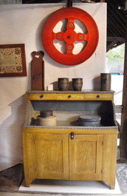 A folky game wheel atop a painted dry sink with three spice drawers and its original zinc liner at Emele's Antiques, Dublin, Penn.