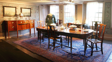 The dining room is furnished with a Massachusetts Hepplewhite mahogany sideboard from the collection of Caroline Emmerton. The set of six New England transitional birch side chairs from about 1760 with bell-shaped rush seats and a vasiform back splat were owned by Susannah Ingersoll and found their way back into the collection. Two China Trade paintings, "View of Macau†and "The Hong of Canton,†were "Found in Collection.†Each bears the stamp of the L.B. Philbrick Company, a late Nineteenth Century supplier of artists' materials in Salem. A pair of circa 1840‱860 Canton tureens is on view in the dining room, along with a circa 1800 platter and an early Nineteenth Century sugar bowl.