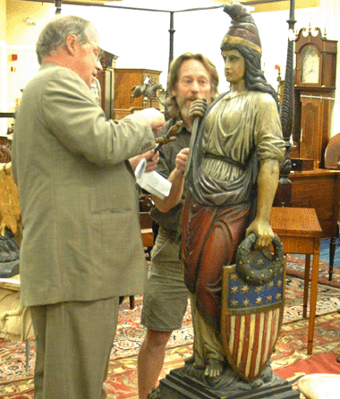 James D. Julia, left, and antiques dealer Don Heller review the features of a rare carved wood figure of the Goddess of Liberty during preview. The life-size polychrome carving showing the American icon holding a sword, laurel wreath and federal shield was the sale's top lot, selling for $143,750 to an unidentified phone bidder.
