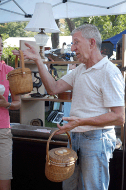 Richard Decker, owner of Longmeddowe Antiques, Monson, Mass., shows off two Nantucket baskets to buyers in his booth. ⁍ay's