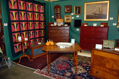 A corn in the field quilt from Wits End Antiques of Wallkill, N.Y., served as the backdrop for a tiger maple drop leaf table, a Chippendale pine chest and a Queen Anne two-drawer blanket chest.
