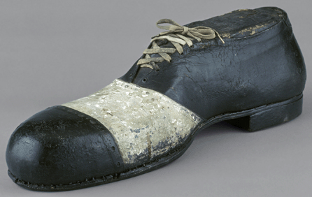 This oversized black and white oxford may have been meant for interior display, as it is painted cardboard and leather. The rubber heel is imprinted with the image of a winged foot, the Goodyear Tire and Rubber company logo. The symbol was first associated with Goodyear's shoe heels in 1914. The sign was probably in use as late as 1920‱940.