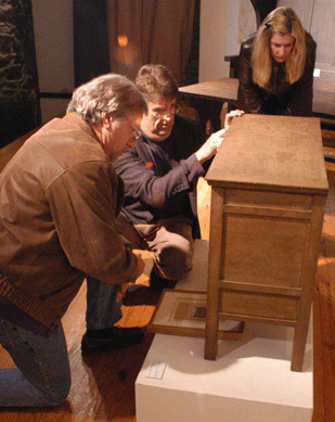 Auctioneer James Bakker, center, looks over a chiffonier made at the Byrdcliffe Arts and Crafts Colony with Two Red Roses founder Rudy Ciccarello prior to an auction in 2005 as Michelle Weinzierl looks on. Ciccarello purchased the rare cabinet with decoration by Hermann Dudley Murphy for a record paid at auction of more than $200,000. ⁁ntiques and the Arts Weekly photo by David S. Smith