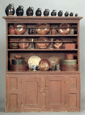 The large step back cupboard in red paint went out at $5,925, a group of ten graduated redware jugs, top, made $2,015, and the "Sally†slipware plate realized $5,925 (Whittemore collection).