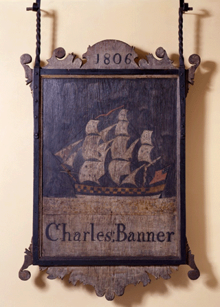 A carved and painted 1806 sign advertising the Charles Banner establishment incorporates the image of a ship under sail and flying the American flag.