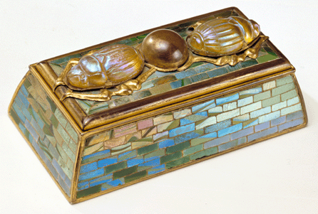 Made of gilt bronze, mosaic glass and molded and pressed glass, the stamp box is jewel-like in its iridescence.