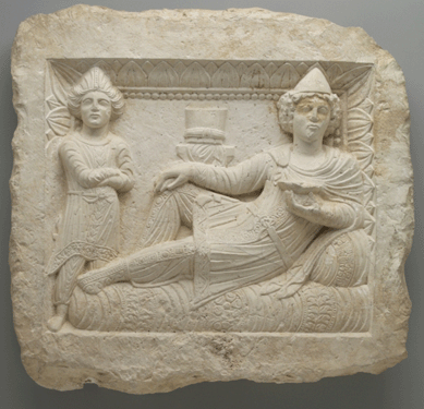 A Palmyrene limestone funerary relief depicts a banquet. The figures themselves and their clothing are highly detailed.