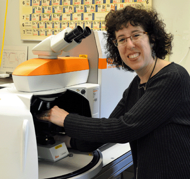 Dr Jennifer L. Mass is pictured with one of the many modern high-tech machines in her department used to analyze chemical content of specimens. Note the periodic table of elements chart behind her on the wall.