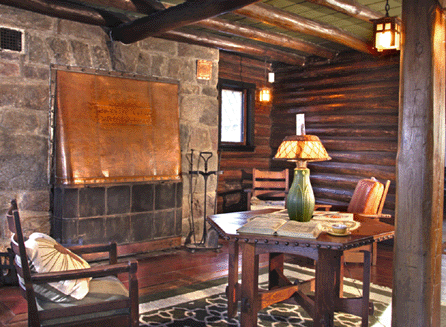 In the living room at Craftsman Farms is a copper hooded fireplace; a Grueby lamp sits atop a hexagonal leather top table and beside it a Morris chair.