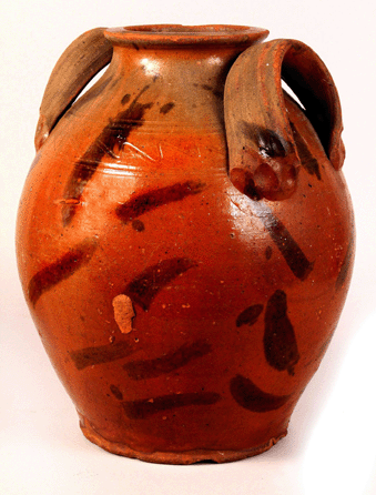 The large redware storage jar has a lead glazed body decorated with manganese stripes, incised sine waving around the upper shoulder and extruded handles, and is attributed to the Cain family of potters of Sullivan County.