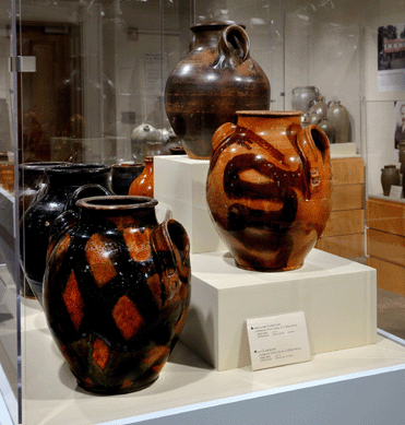 The group of lead glazed earthenware vessels was made in Greene County. The jar at top right was made with handles tucked beneath the rim so that the rim helps support the weight of the pot when lifted. The jar with the snakelike decoration was the first of the Greene County jars unearthed in 1973. The jar decorated with a crosshatch decoration, bottom left, features one stamp on the handle, a mark also noted on the snake jar, both of which are attributed to the Haun Pottery.