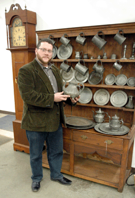 Ryan Brechlin, one of the auctioneers at Nest Egg, with a collection of pewter that was sold November 19. The American tall case clock in cherry, at left, realized $1,652. 