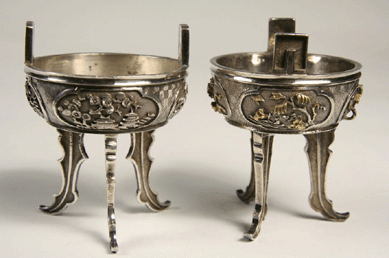 Two Nineteenth Century Chinese silver master salts in archaic form of yoked kettle on triad stand, having deep relief decoration of landscapes with buildings, people, tigers and flowers, brought $25,300.