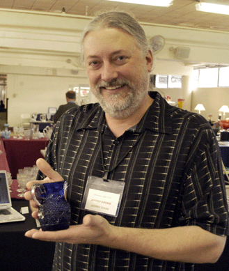 Jeffrey Evans of Jeffrey S. Evans & Associates, Mount Crawford, Va., holds up a rare Sandwich Glass cream pitcher in blue with a clear handle, blown three mold. The auctioneer said only about a half-dozen of this type are known and the creamer will be offered at auction this month.