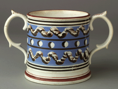 This two-handle mocha cup features a bright blue slip ground with earthworm and cat's-eye motifs. On the interior, three white pierced frogs have been mounted. The holes in them would have produced a whistling sound as the beverage was consumed. Probably Staffordshire, England, circa 1775‱810. Promised gift of Barbara Katz. Courtesy Winterthur.