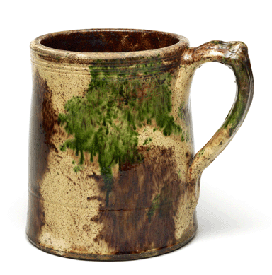 The late Nineteenth Century Shenandoah redware mug is marked "S. Bell & Son, Strasburg.†It is incised with four lines near the rim with a single line lower on the body. Boldly decorated with copper and manganese splotches on a cream slip ground, the mug is typical of Bell's output in the Shenandoah Valley.