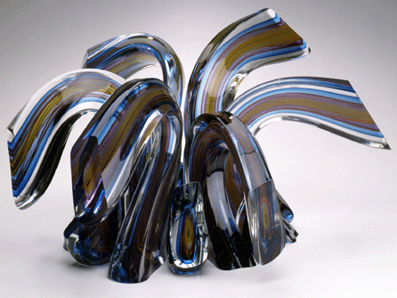 Harvey Littleton, revered as father of the US Studio Glass Movement, is an outstanding artist who pioneered in experimental shaping and coloristic effects in glass. The mesmerizing shapes and color combinations in "Blue/Ruby Spray,†1990, document the skill with which he carried out his philosophy. "When the artist lifts his blowpipe,†Littleton said, "he must be prepared to intervene with all his aptitude, training, form-sense, as well as physical and mental energy. Everything he knows converges at once on this curious scene enacted millions of times in human history: a man breathing his desire into molten glass.†Toledo Museum of Art.