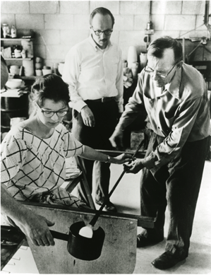 In this photograph from the March 1962 Toledo Workshop, from left, Rosemary Galasso works on molten glass under the watchful eye of leader Harvey Littleton and with the assistance of glassblower Harvey Leafgreen. Toledo Museum of Art.