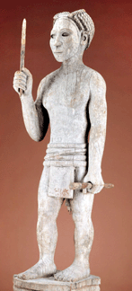 Reminiscent of Greek sculpture, crafted by Sakalava or Bara peoples of Madagascar, this tall wood, pigment and metal funerary sculpture depicting a powerful, armed warrior dates to early to mid-Twentieth Century. It may have been designed as a memorial post or to decorate a tomb.