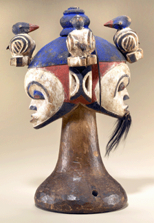 Painted bright blue, red and white and made by Idoma peoples of Nigeria around 1950, this wood mask features female and male faces, topped by birds eating ripe fruit †a reference to harvests. Such crest masks are used at Christmastime, funerals and performances of men's dance groups.
