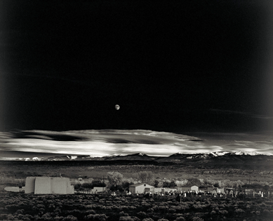 This iconic image, "Moonrise, Hernandez, New Mexico,†1941, was recorded by photographer Ansel Adams late one afternoon when he stopped along a road passing by the village. The moon rising over Hernandez emphasizes its isolation, the expanse of surrounding landscape and the dramatic interplay of light and dark on the horizon. Traugott opines that the picture "symbolizes the triumph of Modernism in New Mexico.• style=