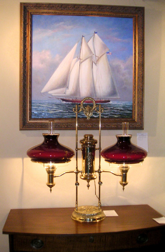 J&M Antiques, East Amherst, N.Y., specializes in antique lighting and period furniture. Their showcase item was a rare double posted table lamp from 1878 that had a matched pair of pigeon blood shades incised with gold decorations. The Twentieth Century oil painting, signed D. Taylor, depicts an American ship flying the national flag.