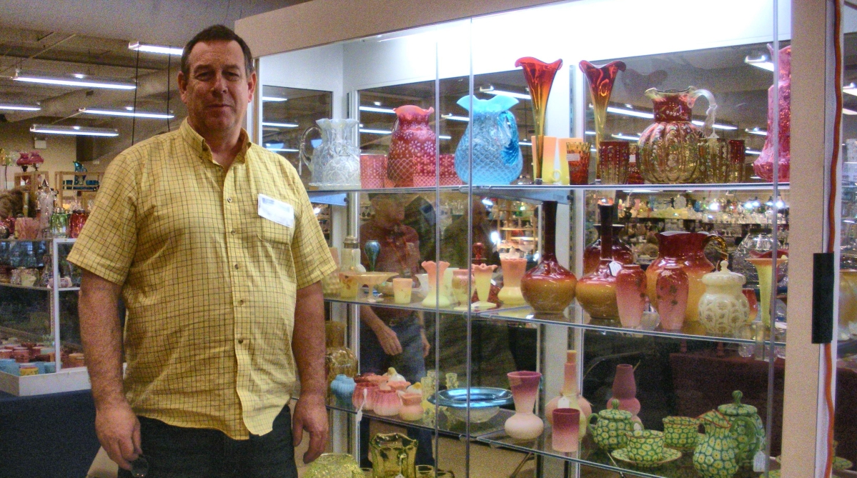 Glimmerglass owner Scott Roland of Schenevus, N.Y., stands next to his display of mostly Victorian art glass, water pitcher sets, tumblers and rare salt shakers.