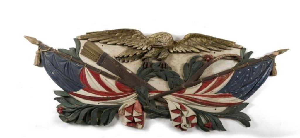 An 81-inch-long carved and painted ship’s sternboard realized $60,000. A displayed eagle was perched on a garland of olive branches above crossed American flags.