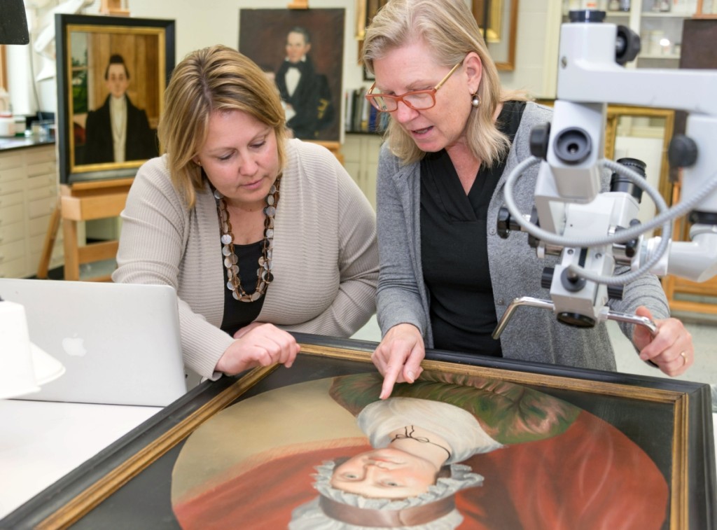 Laura Pass Barry, left, Colonial Williamsburg’s Juli Grainger curator of paintings, drawings and sculpture, and Shelley Svoboda, senior conservator of paintings, examine the circa 1800 portrait of Matilda Morrow by Charles Peale Polk.                                                               —Jason Copes photo