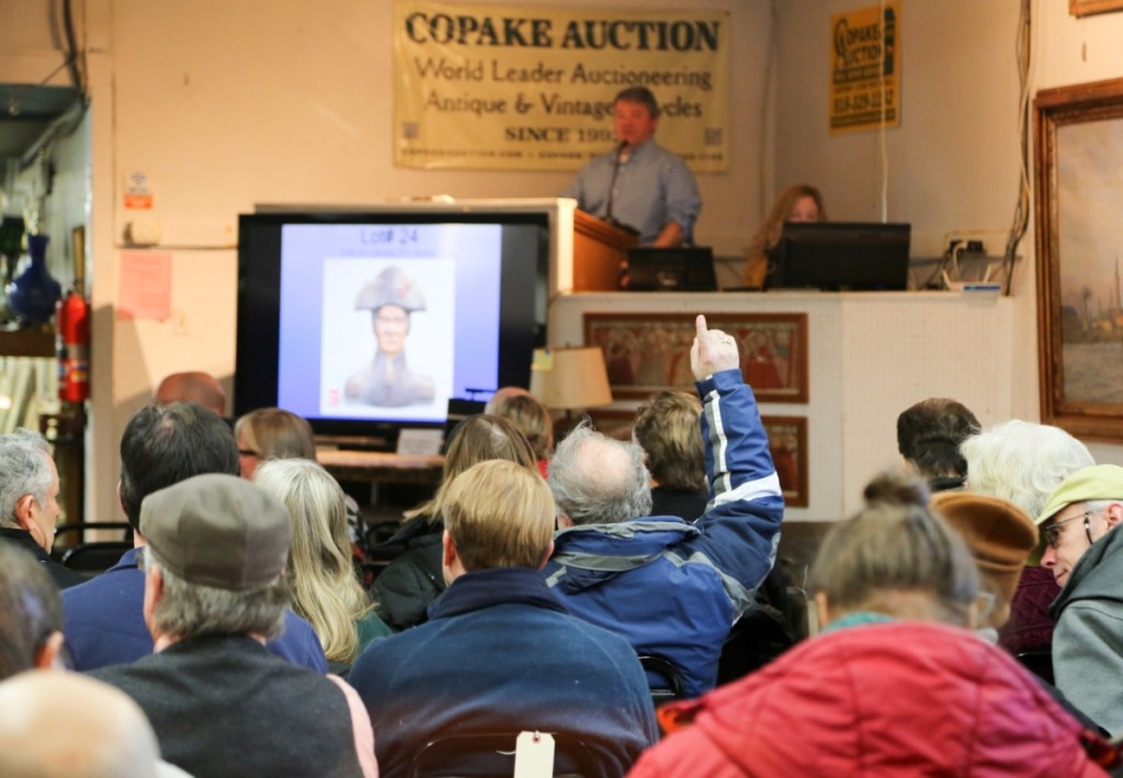 A member of the audience raises his hand high on a folk art carving of a soldier, which brought $1,652, doubling its high estimate.