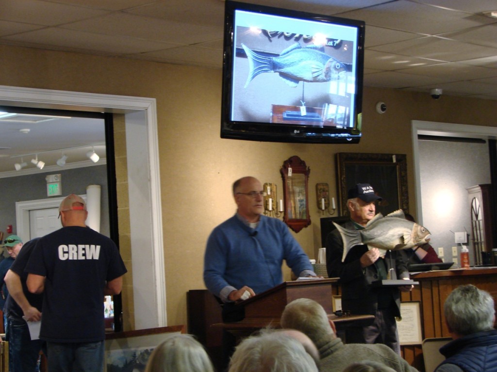 Bill Smith at the podium, selling a tin fish trade sign, with Ken Labnon assisting.