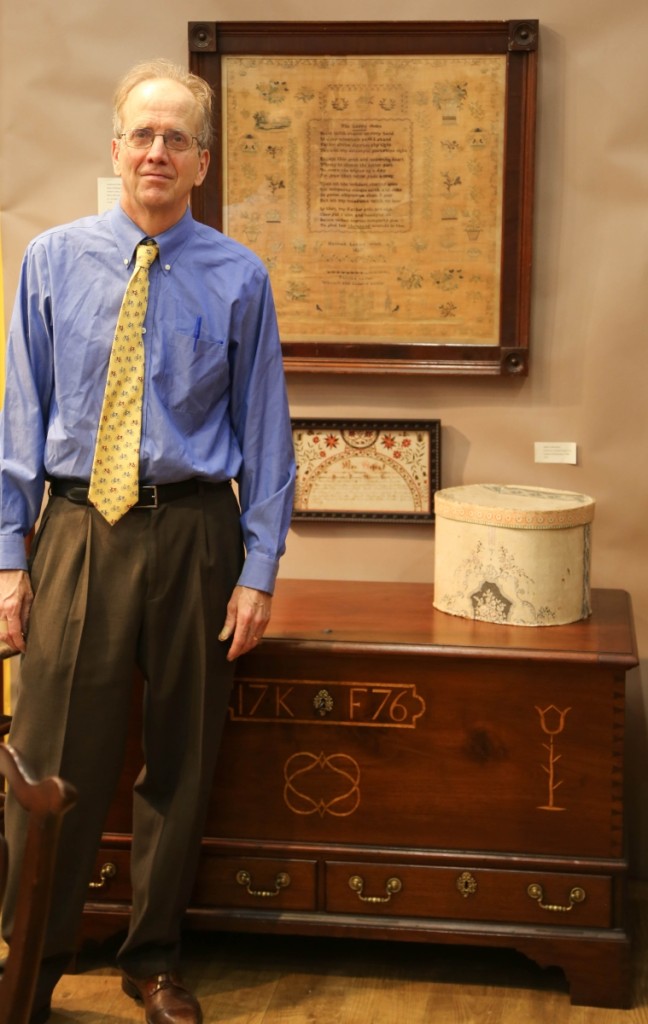 Philip Bradley stands before a 1776 Chester County chest-over-drawers in walnut with mixed-wood inlay. The large 1827 needlework at the top comes in its original mahogany frame and was worked by Hannah Levis (1810–1836).