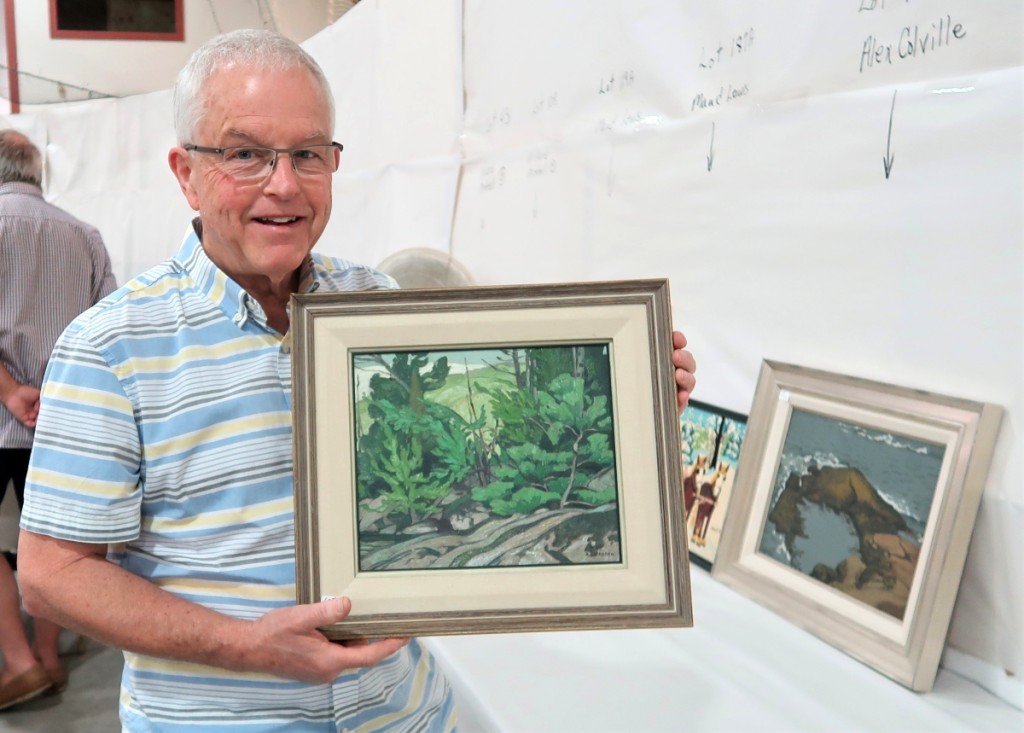 Auctioneer Bill Brayley holds the sale’s top lot, “Lake La Peche,” 1952, a signed and titled oil on canvas by Canadian Group of Seven artist A.J. Casson (1898-1992) that sold for $19,164. Right, “Surf, Peggy’s Cove” by Alex Colville (1920-2013), 1940, made $9,770.