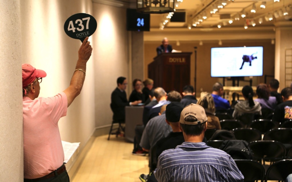 A bidder at the back corner of the room holds his paddle high in the Fall 2019 Asia Week New York.   —Doyle