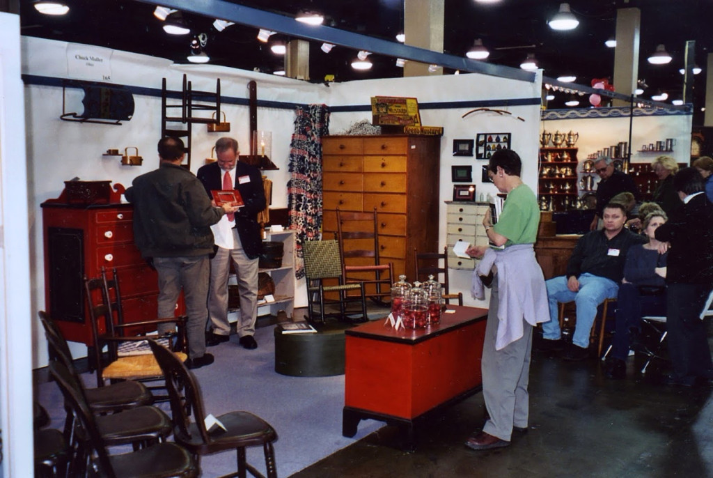 Chuck appears ready to give a lecture in his booth as visitors arrange chairs outside at an unidentified show. The booth is full of Shaker and Soap Hollow examples.