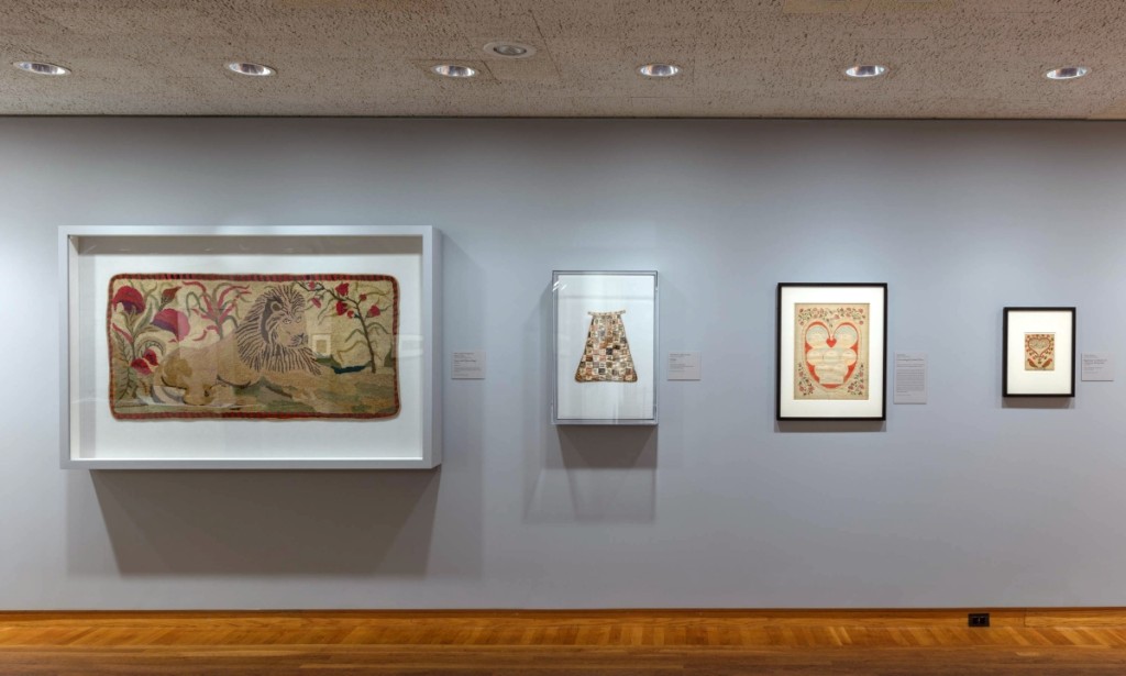 On the wall at left, a hooked rug depicting a recumbent lion after a design by Ebenezer Ross, active 1890-1900. At center right, an 1811 genealogical drawing in ink and watercolor by Lydia Smith.